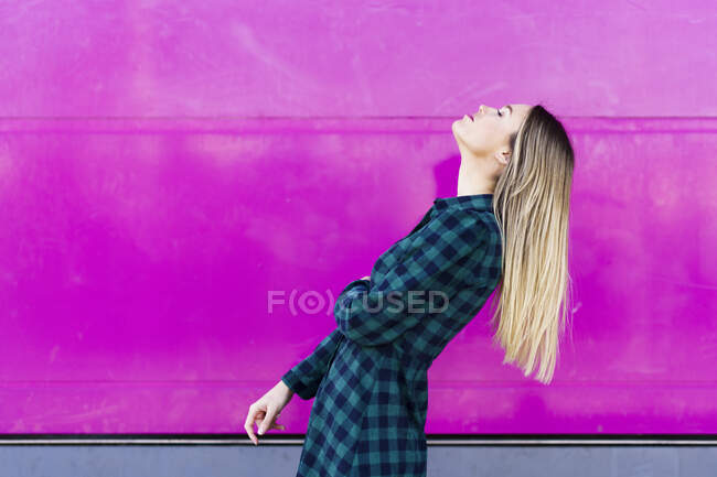 Young woman with head back standing by pink wall — Stock Photo