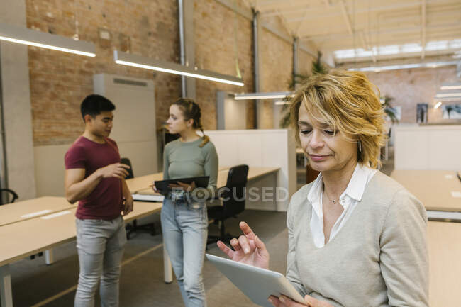 Женщина-предприниматель, использующая цифровой планшет, пока профессионалы обсуждают в офисе — стоковое фото