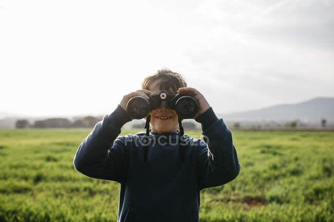 Smiling boy with binoculars in field — Stock Photo