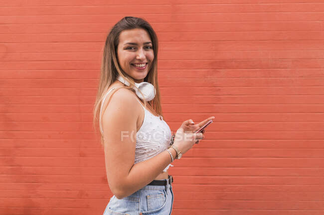 Belle femme avec téléphone portable debout près du mur orange — Photo de stock