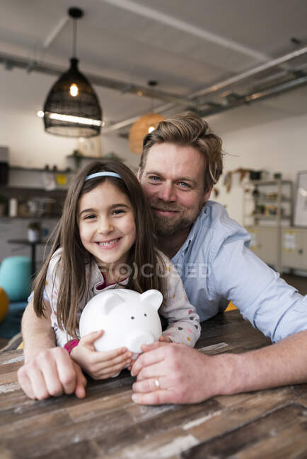 Lächelnder Vater und Tochter mit Sparschwein zu Hause — Stockfoto