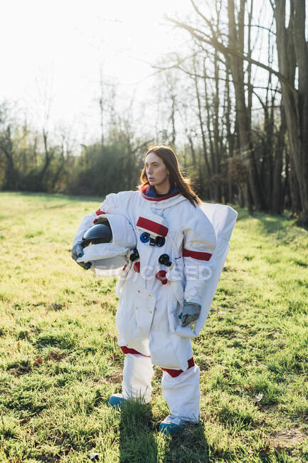 Female astronaut holding space helmet while standing on grass — Foto stock