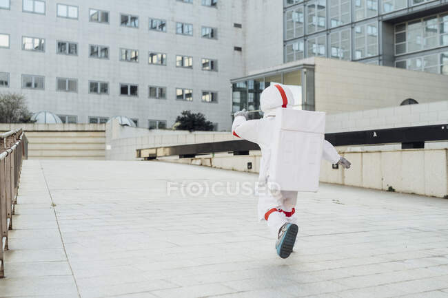 Astronauta corriendo en el paseo marítimo fuera del edificio en la ciudad - foto de stock