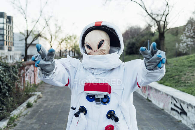 Astronaute femelle avec masque extraterrestre montrant signe de paix tout en se tenant sur le sentier — Photo de stock