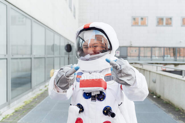 Молодая женщина-астронавт показывает средний палец, стоя возле здания — стоковое фото