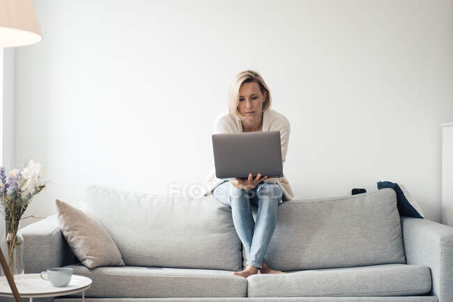 Femme adulte moyenne utilisant un ordinateur portable sur le canapé à la maison — Photo de stock