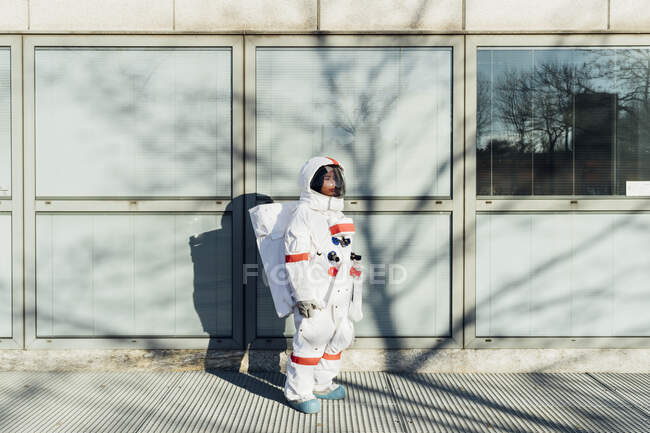 Молодая женщина-астронавт в скафандре, стоящая у окна в городе в солнечный день — стоковое фото