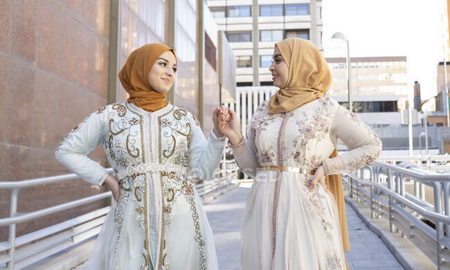 Amis portant hijab et robe souriant tout en tenant la main sur le pont — Photo de stock
