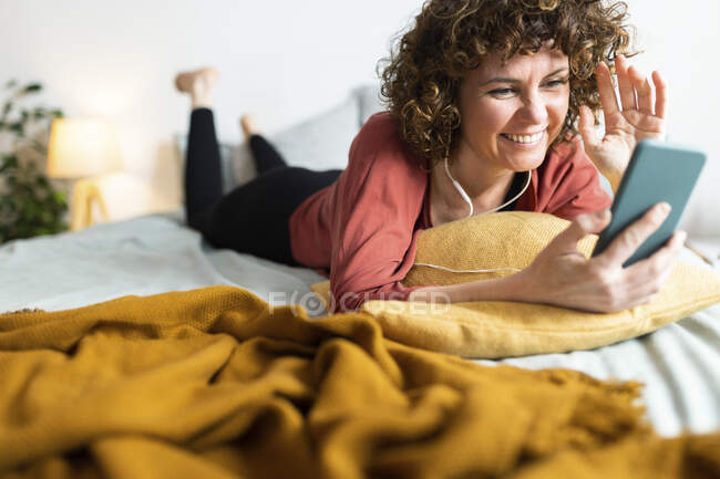 Donna sorridente che fa videochiamata attraverso lo smartphone in camera da letto — Foto stock