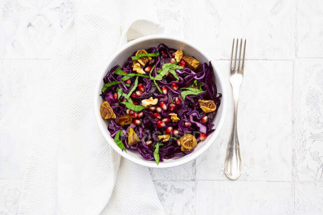 Bowl of vegan salad with red cabbage, pomegranate seeds, dried figs, walnuts and basil — Stock Photo
