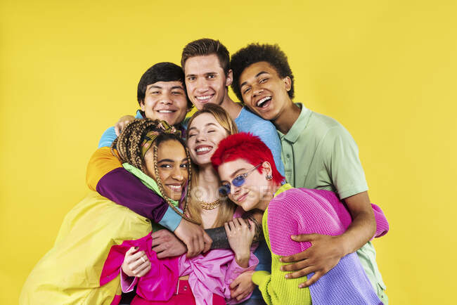 Jóvenes amigos abrazándose mientras están de pie frente al fondo amarillo - foto de stock