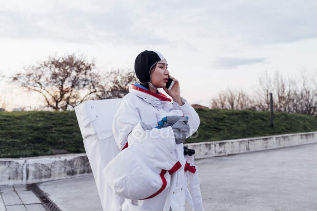 Жіночий космонавт в космічному костюмі розмовляє на смартфоні — стокове фото