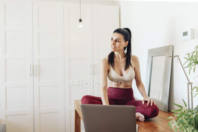 Зрелая женщина смотрит в сторону, сидя с ноутбуком на столе дома — стоковое фото