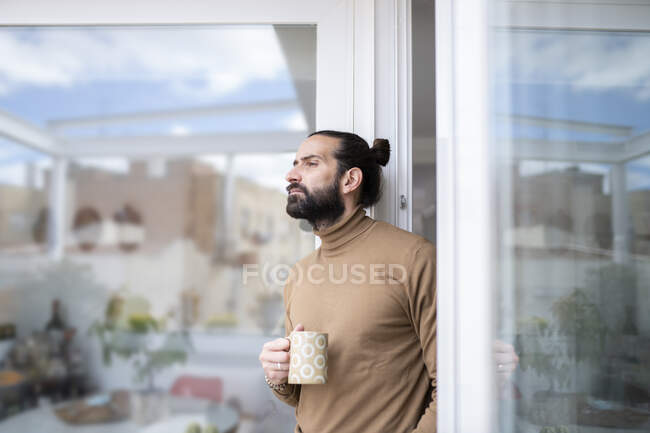 Thoughtful man with mug looking away while standing at doorway — Stock Photo