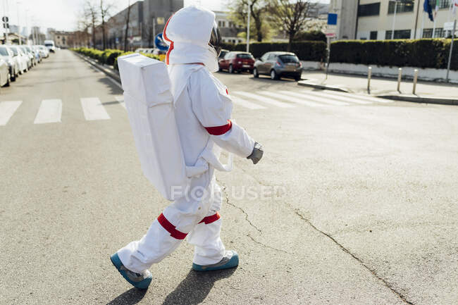 Joven astronauta en traje espacial caminando por la carretera durante el día soleado - foto de stock