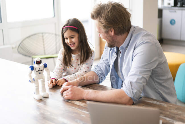 Reifer Mann schaut lächelnde Tochter beim Spielen mit Roboterspielzeug zu Hause an — Stockfoto