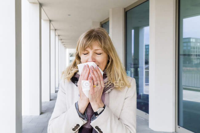 Mature woman sneezing while standing at corridor — Stock Photo