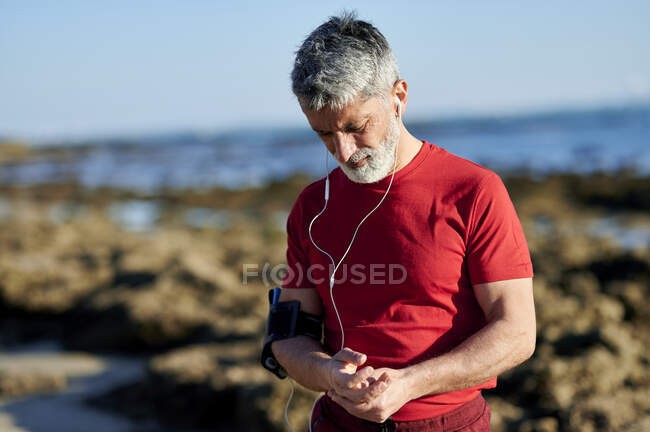 Hombre maduro tocando manos mientras está de pie en la playa - foto de stock