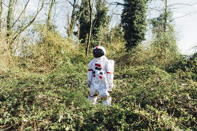 Young astronaut wearing space suit and helmet standing in bush at forest — Stock Photo