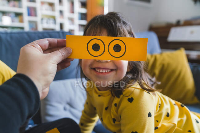 Hombre sosteniendo emoticono amarillo sobre la cara de la chica sonriente en casa - foto de stock