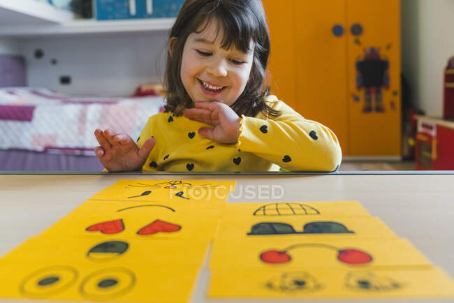 Chica feliz arreglando emoticonos en la mesa en la sala de juegos en casa - foto de stock