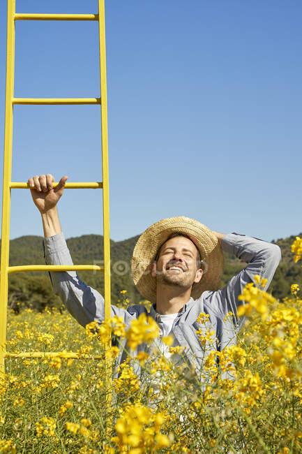 Smiling man with head in hand holding ladder in field — Stock Photo