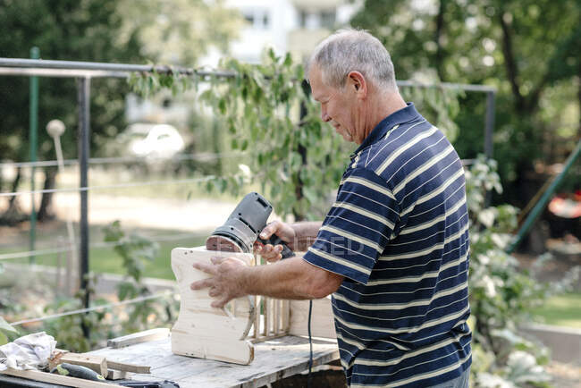 Hombre mayor activo con herramienta de carpintería haciendo carpintería en el patio trasero - foto de stock