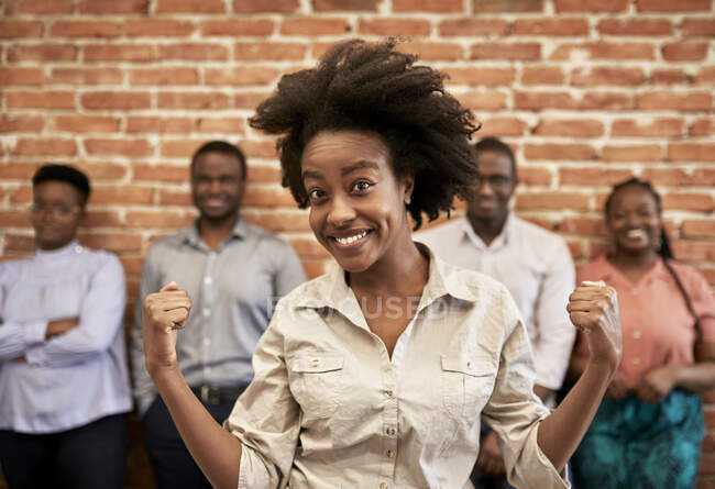 Femme d'affaires souriante fléchissant les muscles avec des collègues masculins et féminins en arrière-plan au bureau — Photo de stock