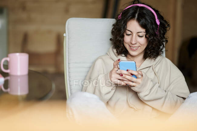 Mujer feliz escuchando música mientras usa el teléfono inteligente en casa - foto de stock