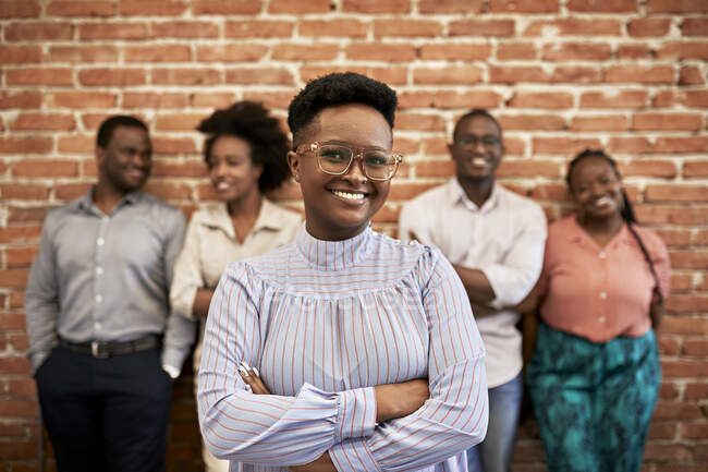 Smiling businesswoman wearing eyeglasses with coworkers standing in background at office — Stock Photo