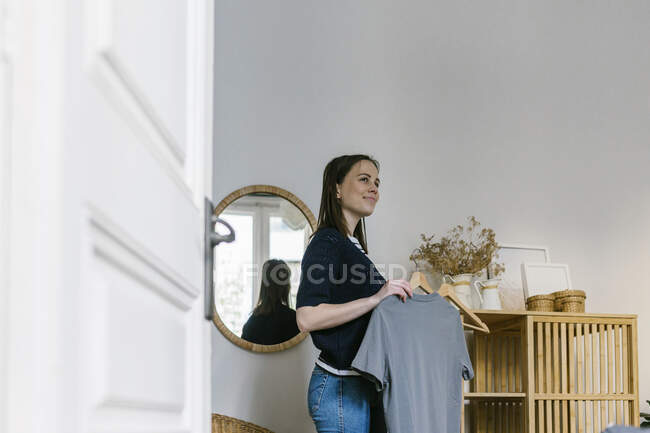 Donna sorridente contemplando mentre tiene i vestiti in casa di vacanza — Foto stock