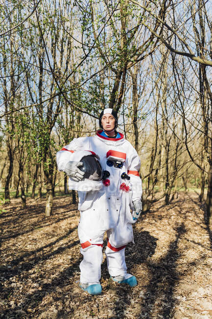Female astronaut holding space helmet while standing in forest — Fotografia de Stock