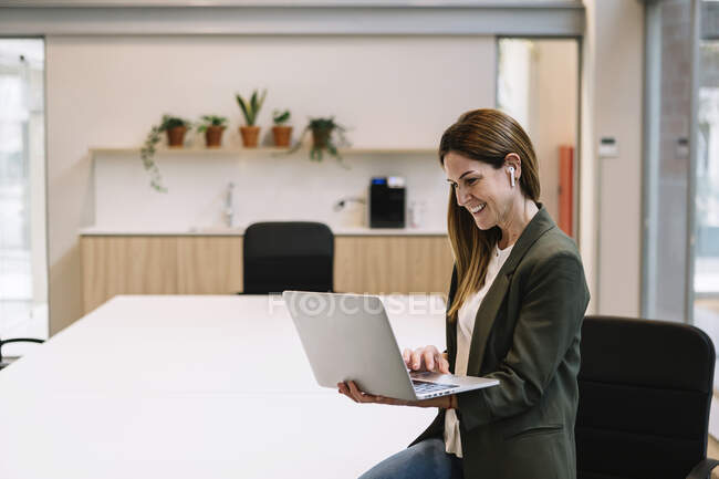 Lächelnde Unternehmerin mit In-Ear-Kopfhörern mit Laptop im Büro — Stockfoto