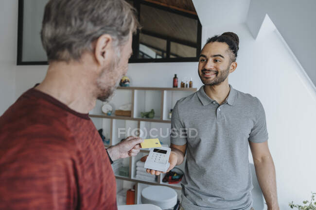 Smiling physiotherapist holding credit card reader in medical practice — Stock Photo