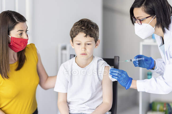Мать утешает сына, принимающего вакцину COVID от женщины-врача в клинике — стоковое фото