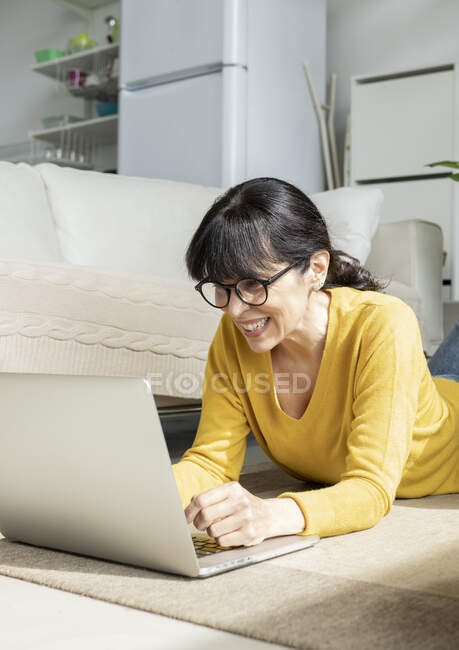Donna sorridente che utilizza il computer portatile mentre si trova sul pavimento a casa — Foto stock