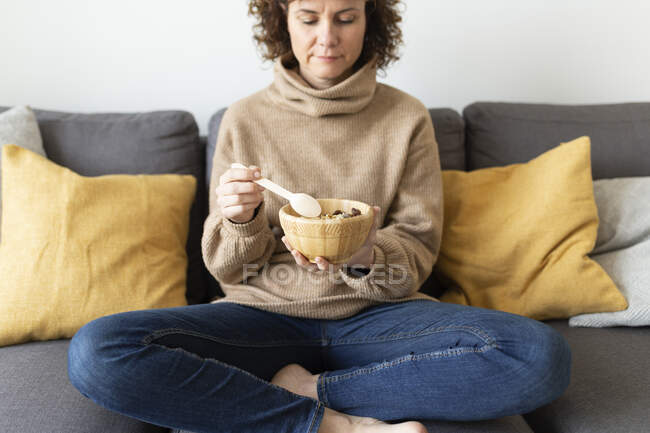Зрелая женщина завтракает, сидя дома на диване — стоковое фото