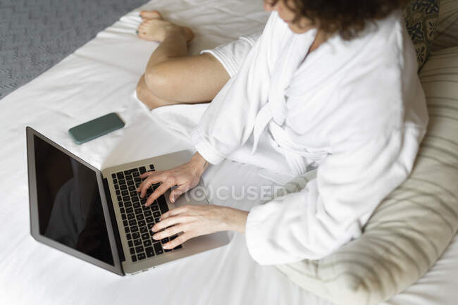 Femme d'affaires mature en peignoir travaillant sur ordinateur portable dans la chambre d'hôtel — Photo de stock