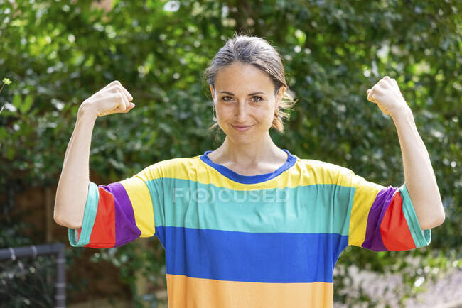 Hermosa mujer adulta mediana que usa bíceps de flexión superior multicolor en el jardín - foto de stock
