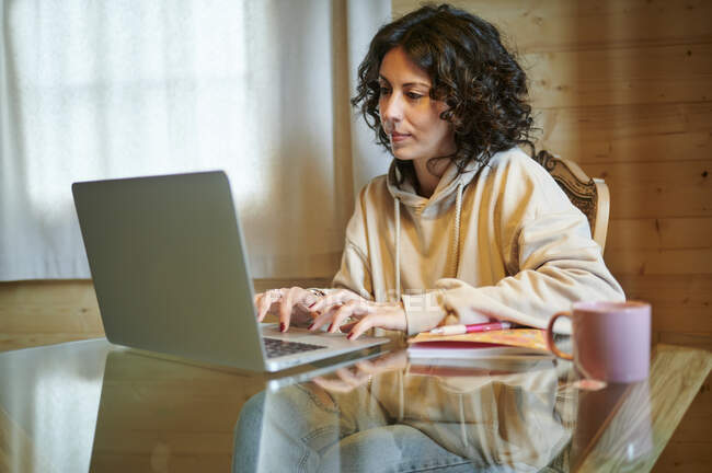 Femme aux cheveux bouclés utilisant un ordinateur portable à la maison — Photo de stock