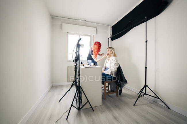 Female make-up artist applying face powder on model while blogging at studio — Stock Photo