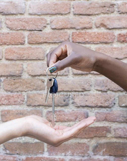 Young woman giving keys to friend by brick wall — Stock Photo