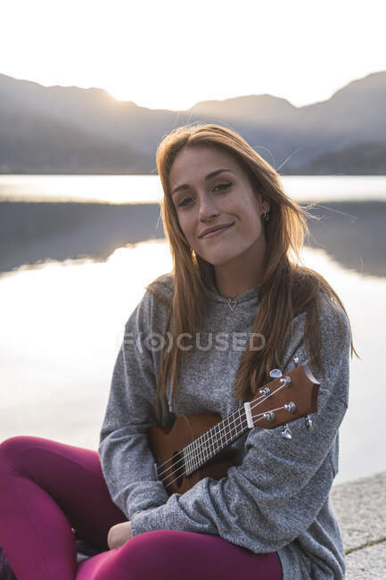 Donna felice con ukulele seduta sulla riva del lago — Foto stock