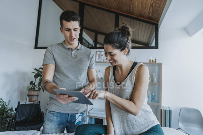 Smiling female patient with physiotherapist looking at digital tablet in medical practice — Foto stock