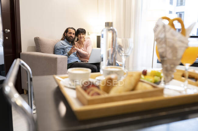 Усміхнений чоловік вказує на сніданок жінкою в готельному номері — стокове фото