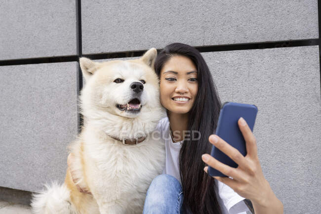 Hipster donna prendere selfie con Akita cane attraverso il telefono cellulare da parete — Foto stock