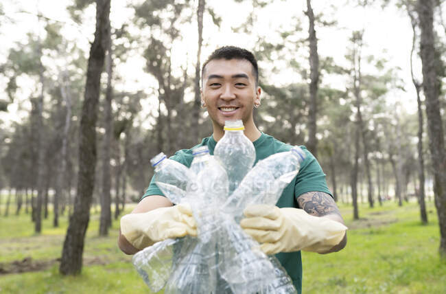 Эколог улыбается, держа пластиковые бутылки в лесу — стоковое фото