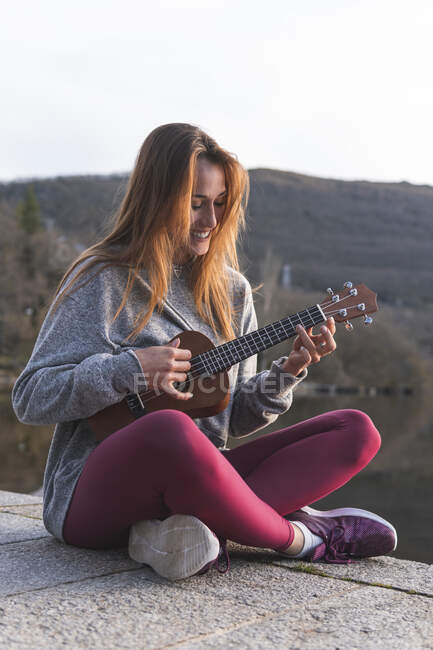 Bella donna giocare ukulele su mentre seduto sul lungomare — Foto stock