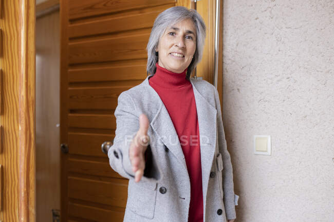 Mujer sonriente en chaqueta ofreciendo apretón de manos en la puerta principal de la casa - foto de stock
