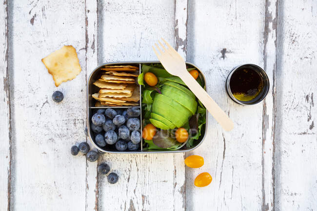 Lunchbox avec salade, avocat et tomates jaunes, craquelins, bleuets et vinaigrette — Photo de stock